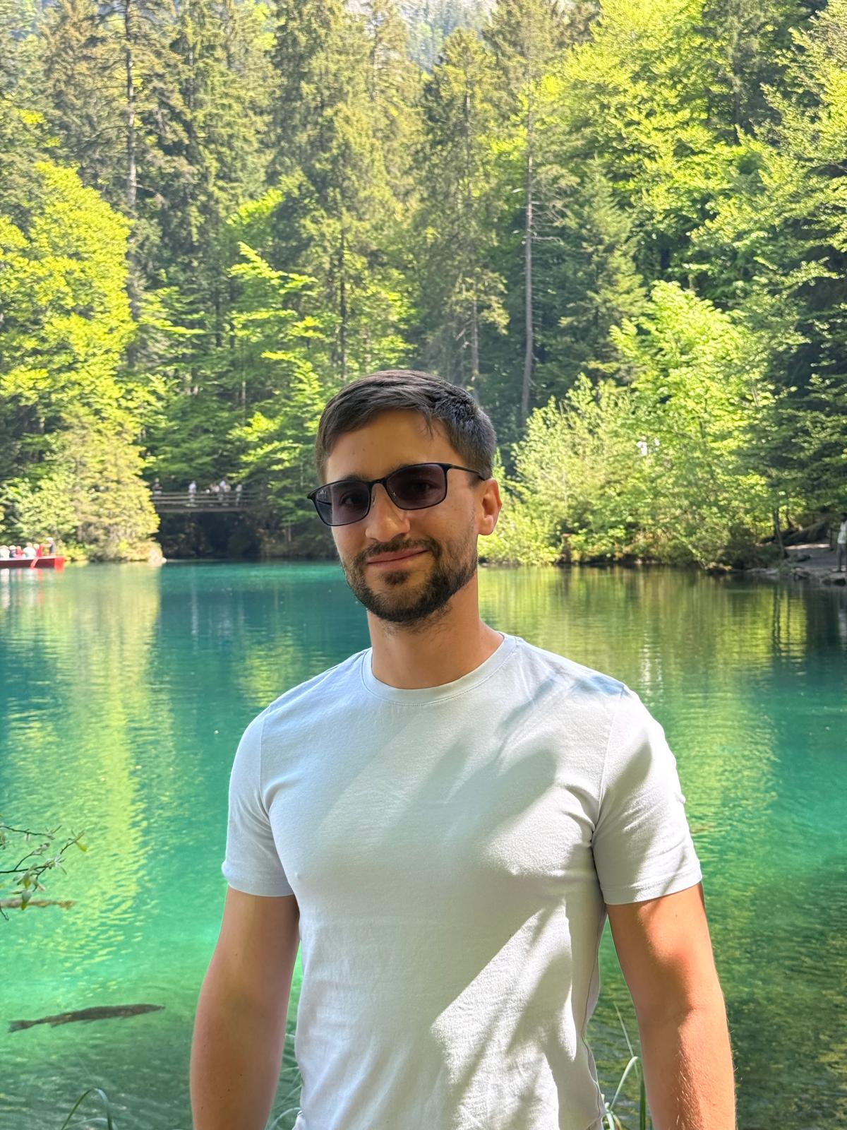 Alfonso beside a turquoise alpine lake surrounded by forest